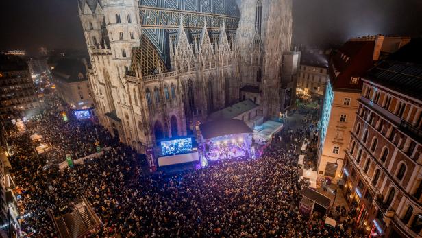 Große Menschenmenge versammelt sich bei Nacht vor einem beleuchteten Dom mit Bühne und Leinwand in einer Innenstadt.