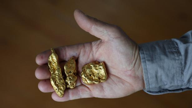 A shop worker poses holding three gold nuggets at The Gold Centre store, in Maryborough