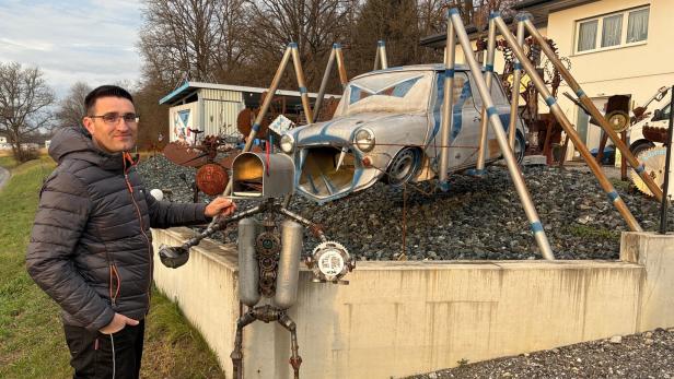 Ein Mann steht neben einer skurrilen Metallskulptur, im Hintergrund ein Auto mit Spinnenbeinen aus Metall.