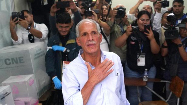 Nasry Asfura steht in einem Wahllokal. Hinter ihm sind viele Reporter mit Kameras, die auf ihn gerichtet sind.