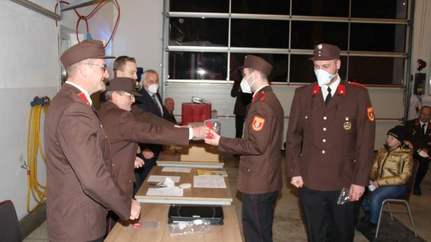 Feuerwehrmänner in Uniform übergeben sich gegenseitig ein verpacktes Geschenk.