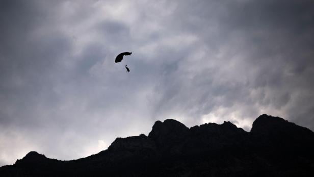 Ein Fallschirmspringer schwebt vor dunklen Bergen unter bewölktem Himmel.