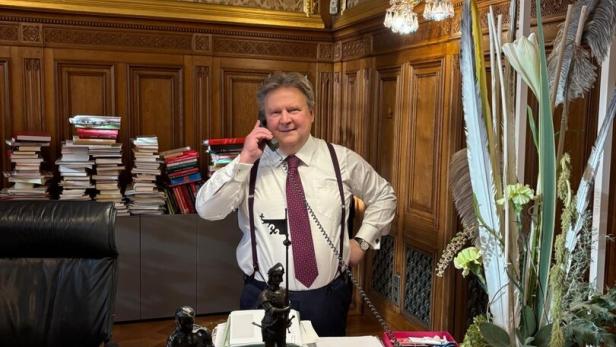 Wiens Bürgermeister Michael Ludwig telefoniert in einem prunkvoll eingerichteten Büro mit vielen Aktenstapeln und Dekoration auf dem Schreibtisch.