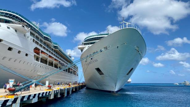Zwei große Kreuzfahrtschiffe liegen bei sonnigem Wetter an einem Pier im türkisblauen Wasser.