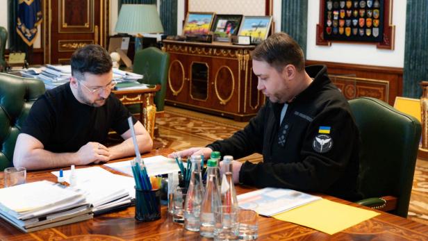 Zwei Männer sitzen an einem Tisch mit Papieren und Wasserflaschen in einem Büro.