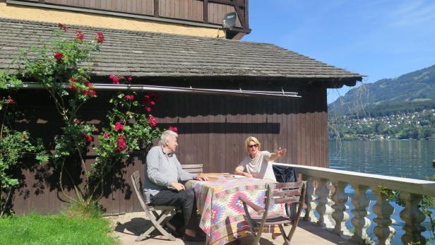 Ein Mann und eine Frau sitzen an einem Tisch auf einer Terrasse mit Blick auf einen See.