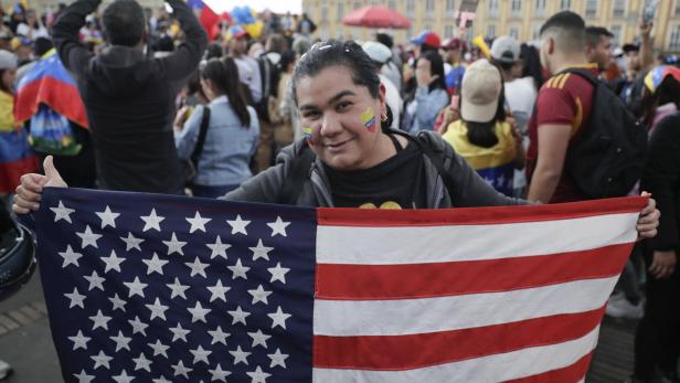 Eine Person hält eine US-Flagge vor einer Menschenmenge, mit venezolanischen Flaggen auf ihren Wangen gemalt.