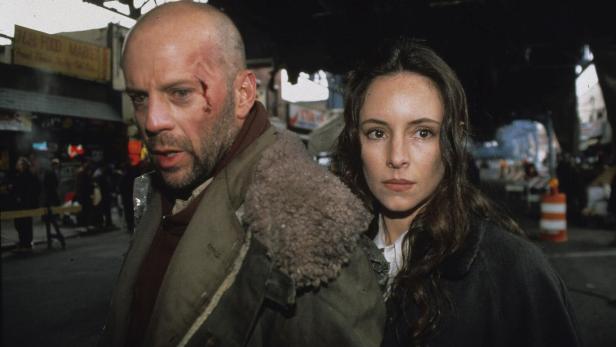 Ein Mann mit einer Wunde im Gesicht und eine Frau stehen ernst nebeneinander auf einer belebten Straße.