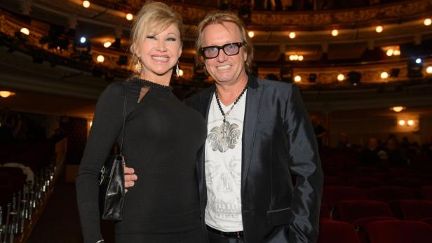 Ein lächelndes Paar in eleganter Kleidung steht in einem festlich beleuchteten Theatersaal.