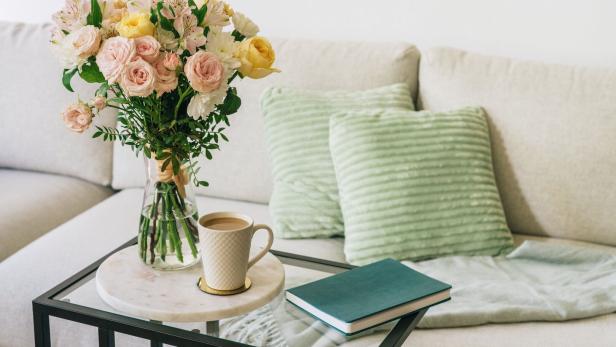 Coffee cup, flowers, and notebook on a glass table next to a couch