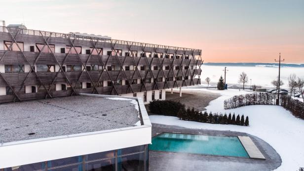 Ein Hotelgebäude mit großem Außenpool in winterlicher Landschaft mit Schnee.