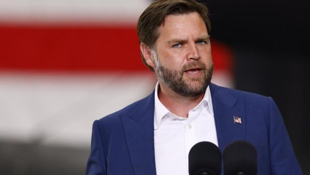 JD Vance spricht vor Mikrofonen, eine US-Flagge ist an seinem Revers befestigt.