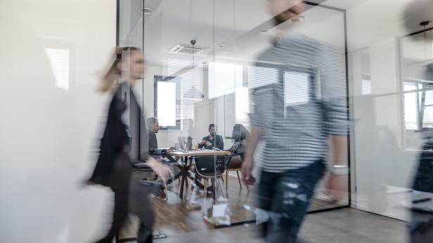 Im Büro gehen verschwommene Personen vorbei, während andere an einem Tisch sitzen.