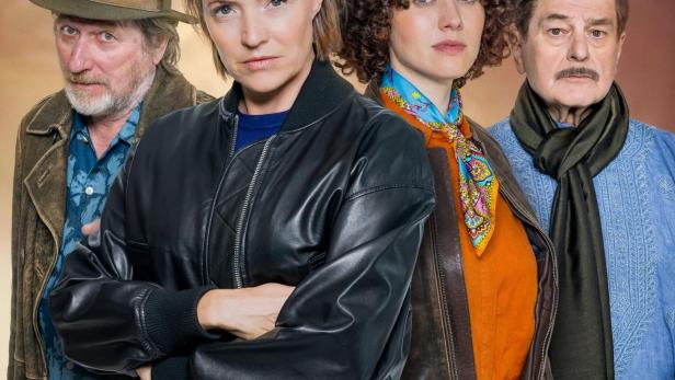 Vier Erwachsene stehen nebeneinander, jeder mit unterschiedlichem Gesichtsausdruck und individueller Kleidung.