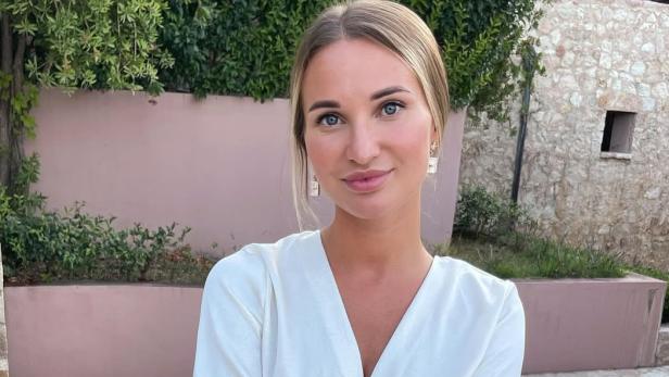 38-jährige blonde Frau mit weißer Bluse posiert lächelnd für ein Foto