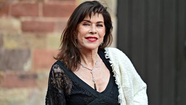 Frau mit dunklen Haaren trägt ein schwarzes Spitzenkleid, eine weiße Stola und eine silberne Halskette.