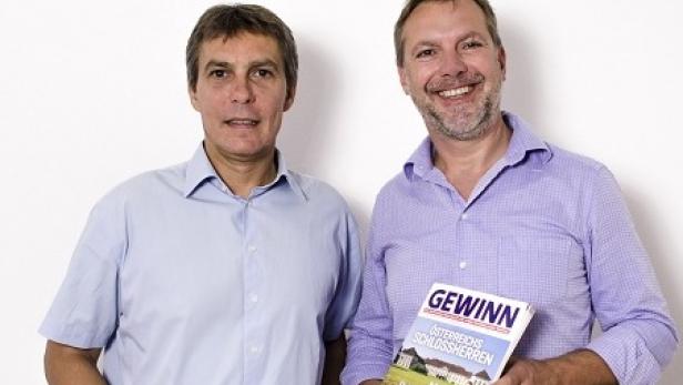 Zwei Männer posieren mit Zeitschriften vor einer weißen Wand.