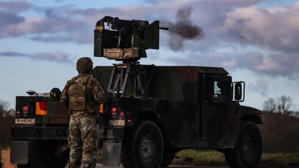 Ein Soldat in Tarnuniform steht neben einem Militärfahrzeug mit montiertem, schießendem Maschinengewehr.