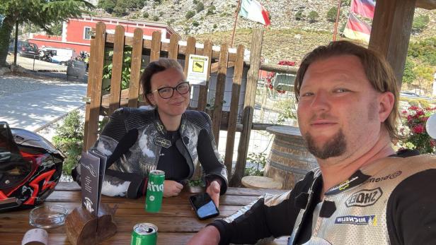 Ein Mann und eine Frau in Biker-Kleidung sitzen an einem Tisch und machen ein Selfie.