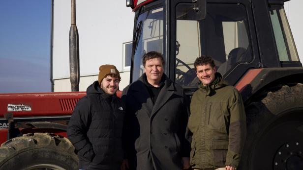 Drei Männer stehen vor einem roten Traktor auf einem Feld.