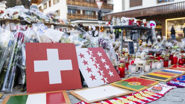Blumen, Kerzen und Flaggen, darunter die Schweizer Flagge, liegen auf einem Platz.