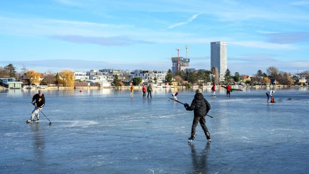 Mehrere Menschen spielen Eishockey und laufen Schlittschuh auf der zugefrorenen Alten Donau