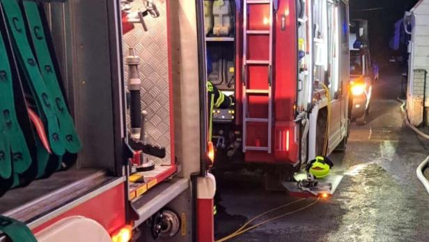Zwei Feuerwehrfahrzeuge mit angeschlossenen Schläuchen und Ausrüstung stehen nachts auf einer nassen Straße.