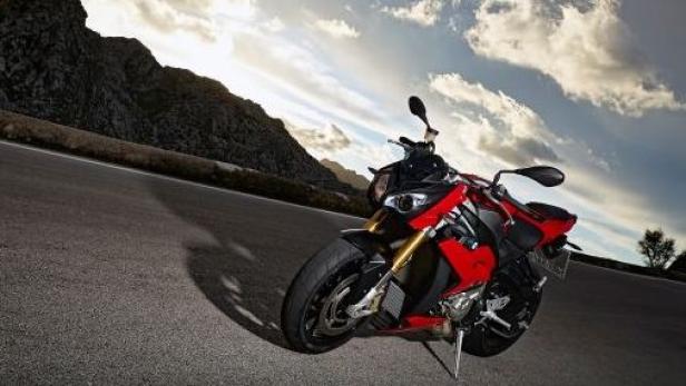 Ein rotes Motorrad steht auf einer Landstraße vor einer Bergkulisse.