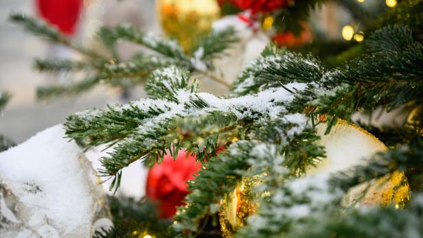 Schnee bedeckt die Zweige eines Weihnachtsbaums mit roten und goldenen Kugeln.