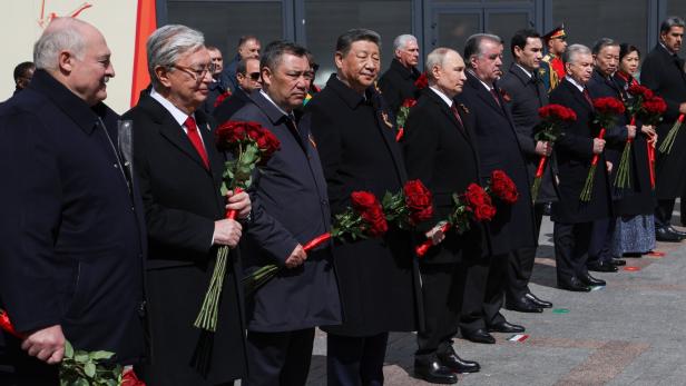 Mehrere Männer in dunklen Mänteln stehen nebeneinander und halten rote Rosensträuße in den Händen.