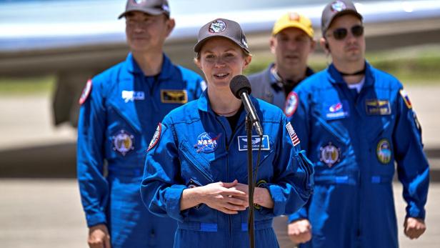 Eine NASA-Astronautin spricht am Mikrofon, umgeben von drei weiteren Personen in blauen Overalls.