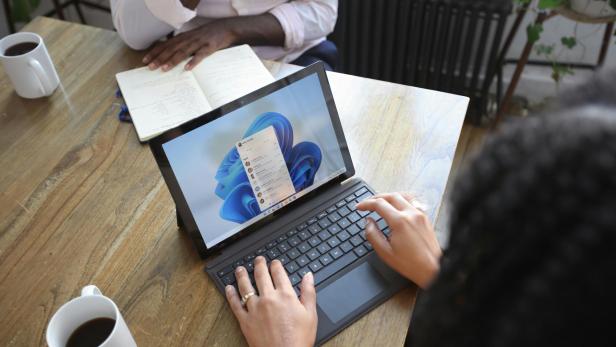 Zwei Personen sitzen am Tisch und arbeiten. Eine Person mit einem Laptop