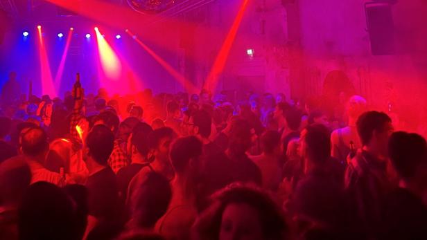 Viele Menschen tanzen in einem Club mit bunten Lichtern, Nebel und einer Discokugel an der Decke.