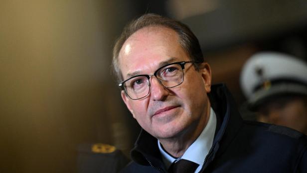 Dobrindt blickt in die Kamera, im Hintergrund eine Person mit Uniformmütze.