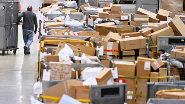 In einem Lager zieht ein Mann einen Wagen, während andere Wagen mit Paketen gefüllt sind.