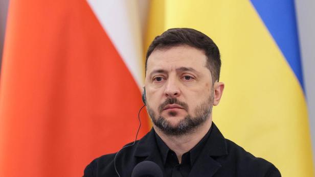 Wolodymyr Selenskyj mit Headset vor den Flaggen der Ukraine und Polens.