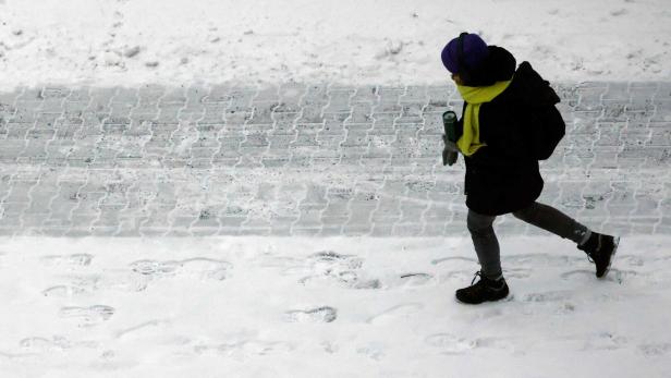 Ein Mensch geht auf einer winterlichen, teils mit Schnee bedeckten Straße.