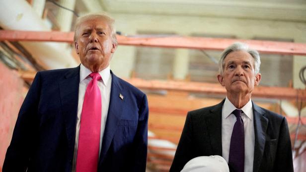 Donald Trump und Jerome Powell stehen nebeneinander, Powell hält einen weißen Bauhelm.