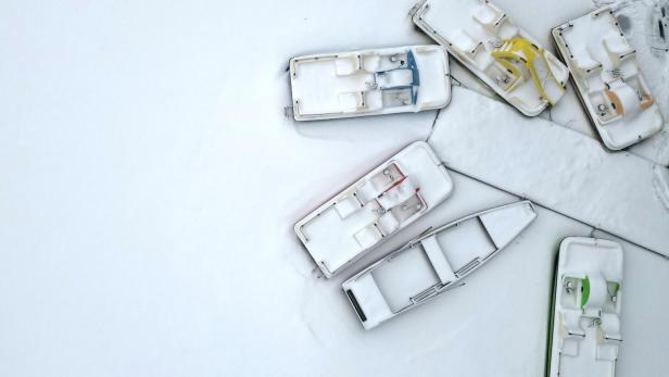 Mehrere schneebedeckte Boote in verschiedenen Farben liegen auf einer weißen Oberfläche.