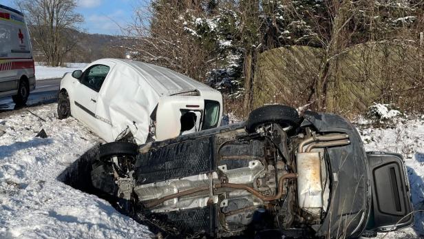 Zwei beschädigte Fahrzeuge liegen im verschneiten Straßengraben, ein Rettungswagen steht daneben.