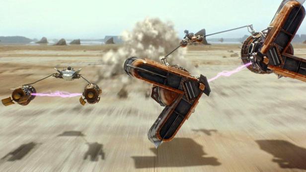 Zwei futuristische Rennfahrzeuge rasen mit hoher Geschwindigkeit über eine sandige Wüstenlandschaft.