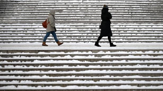 Zwei Personen in Winterkleidung gehen an verschneiten Treppenstufen vorbei.