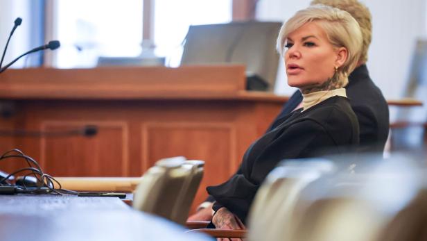 Eine Frau mit kurzem blondem Haar und sichtbaren Tattoos sitzt in einem Gerichtssaal auf einem Stuhl.