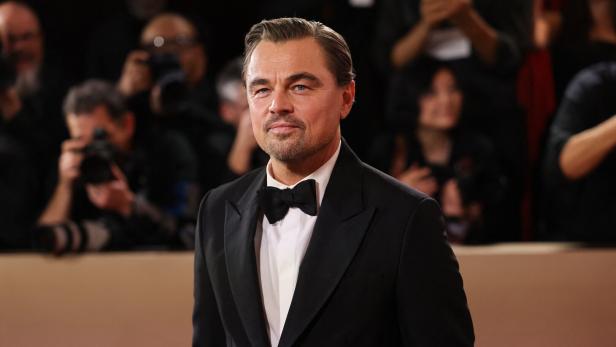 Leonardo DiCaprio trägt einen Smoking und eine Fliege vor einer Menge mit Kameras.