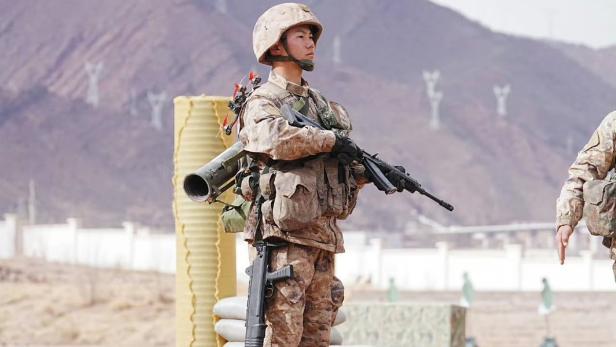 Chinesischer Soldat mit Sturmgewehr, Schrotflinte, Raketenwerfer und Drohne auf einem Übungsplatz.