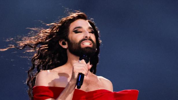 Conchita Wurst singt in einem roten Kleid mit Bart und wallendem Haar.