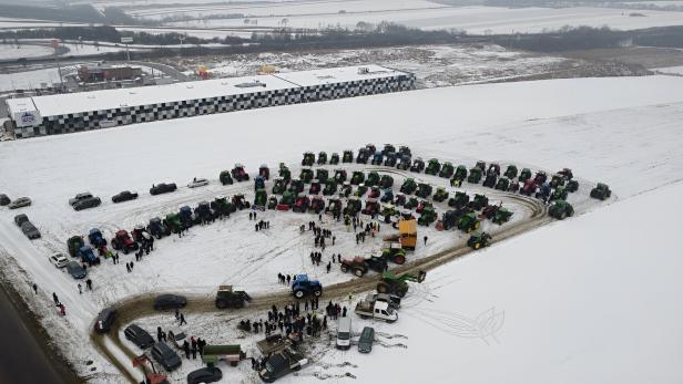 Viele Traktoren und Menschen versammeln sich auf einem verschneiten Feld in einer großen Kreisformation.