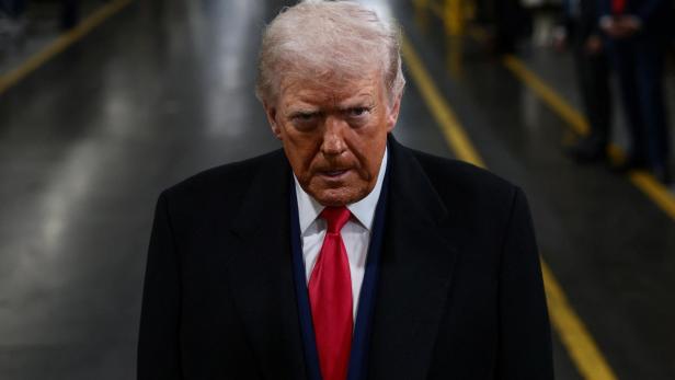 Donald Trump blickt ernst in die Kamera, gekleidet in einen dunklen Mantel und eine rote Krawatte.