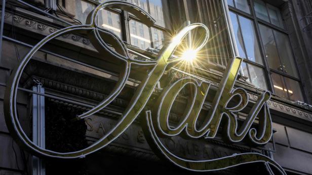 Ein goldenes "Saks"-Schild leuchtet an der Fassade eines Gebäudes mit Fenstern.