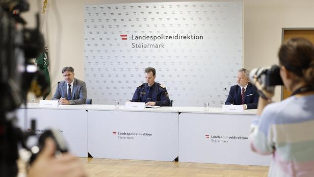 Drei Männer sitzen bei einer Pressekonferenz der Landespolizeidirektion Steiermark an einem Tisch, eine Frau fotografiert sie.